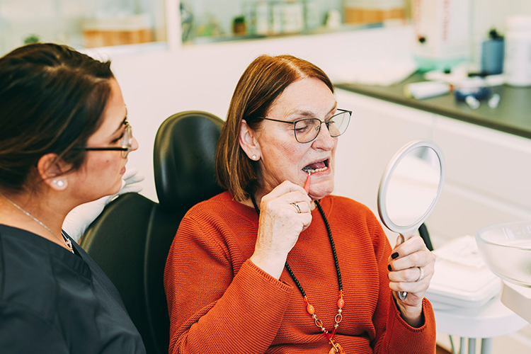 Eine Patientin schaut sich ihre Zähne im Spiegel, nach einer Prophylaxebehandlung an, in der Zahnarztpraxis Matthias Theel in Hilpoltstein